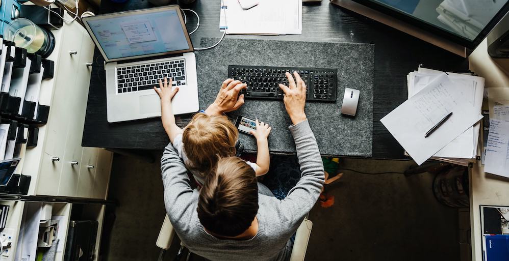 a man holds his son in his lap. they're both typing on different laptops